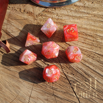Set of red rose pink swirly pearl polyhedral dice with gold numbers on a wooden surface