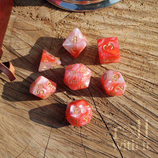 Set of red rose pink swirly pearl polyhedral dice with gold numbers on a wooden surface