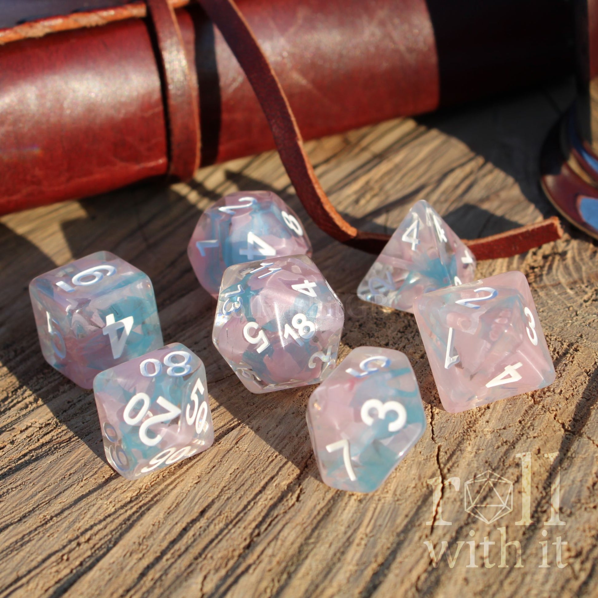 Side view of 7 cute fantasy aesthetic pink blue swirling polyhedral TTRPG dice on a wooden surface