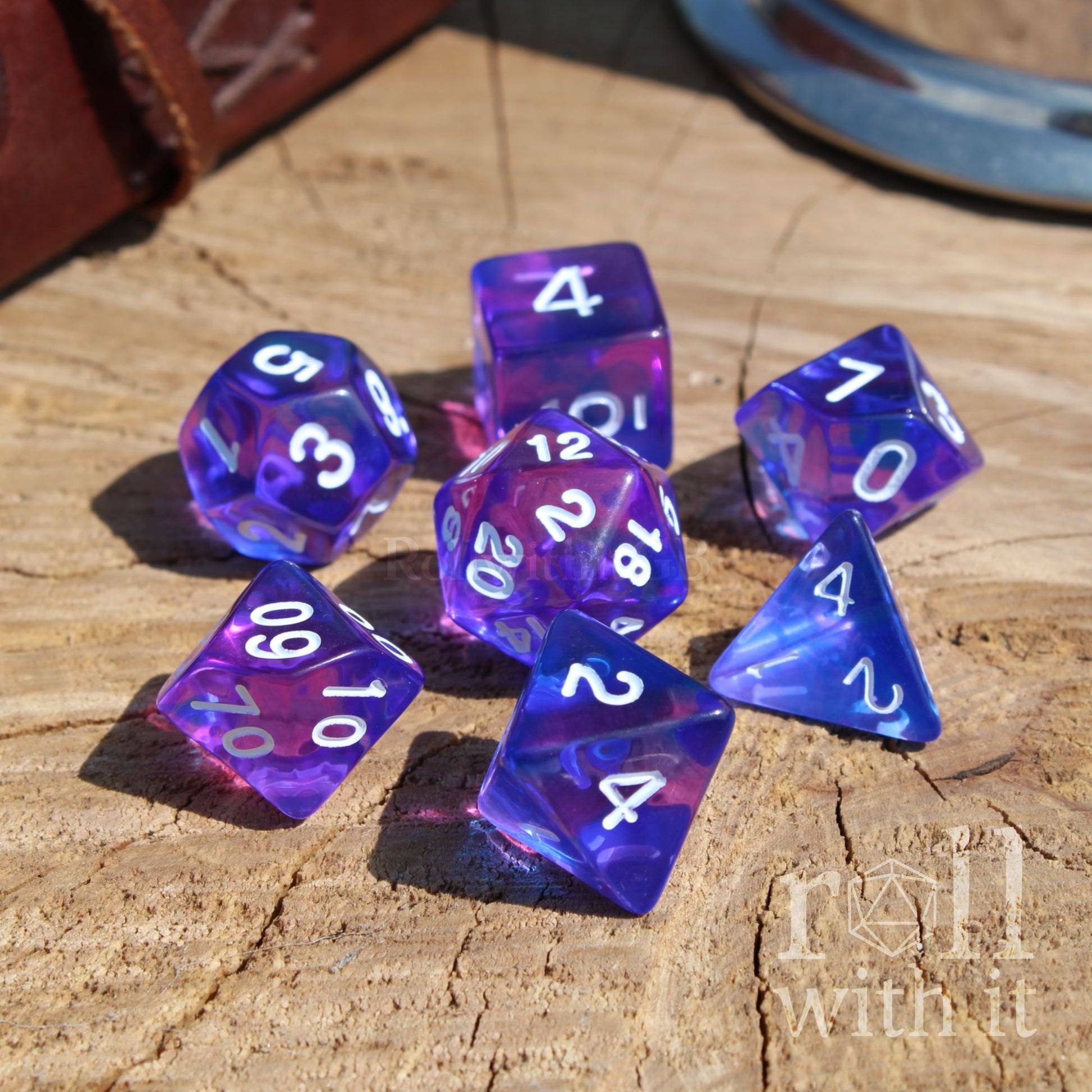 Purple and blue polyhedral dice set on a wooden surface with 'roll with it' branding.