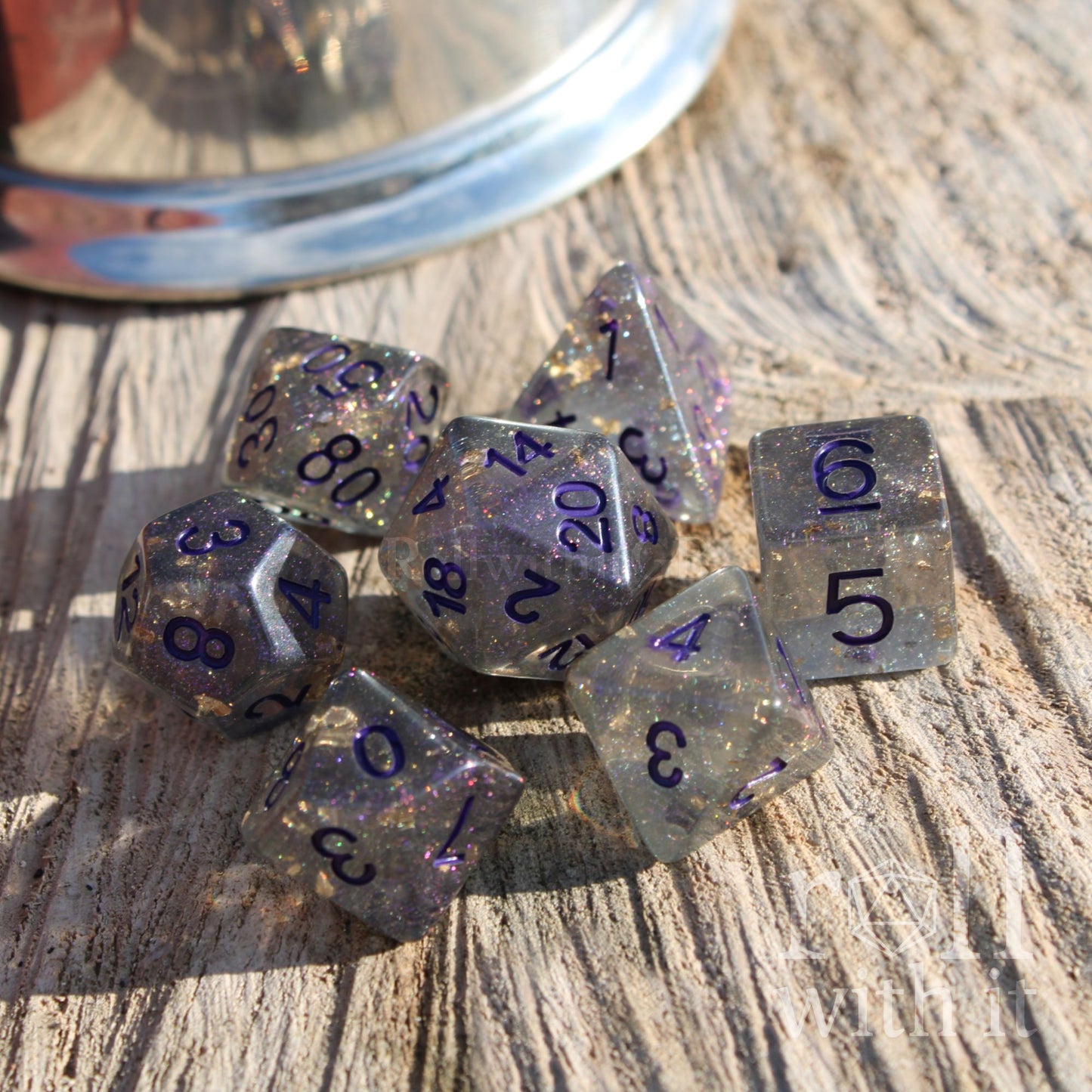 Set of grey sparkling gold foil polyhedral dice with purple numbers on a wooden surface