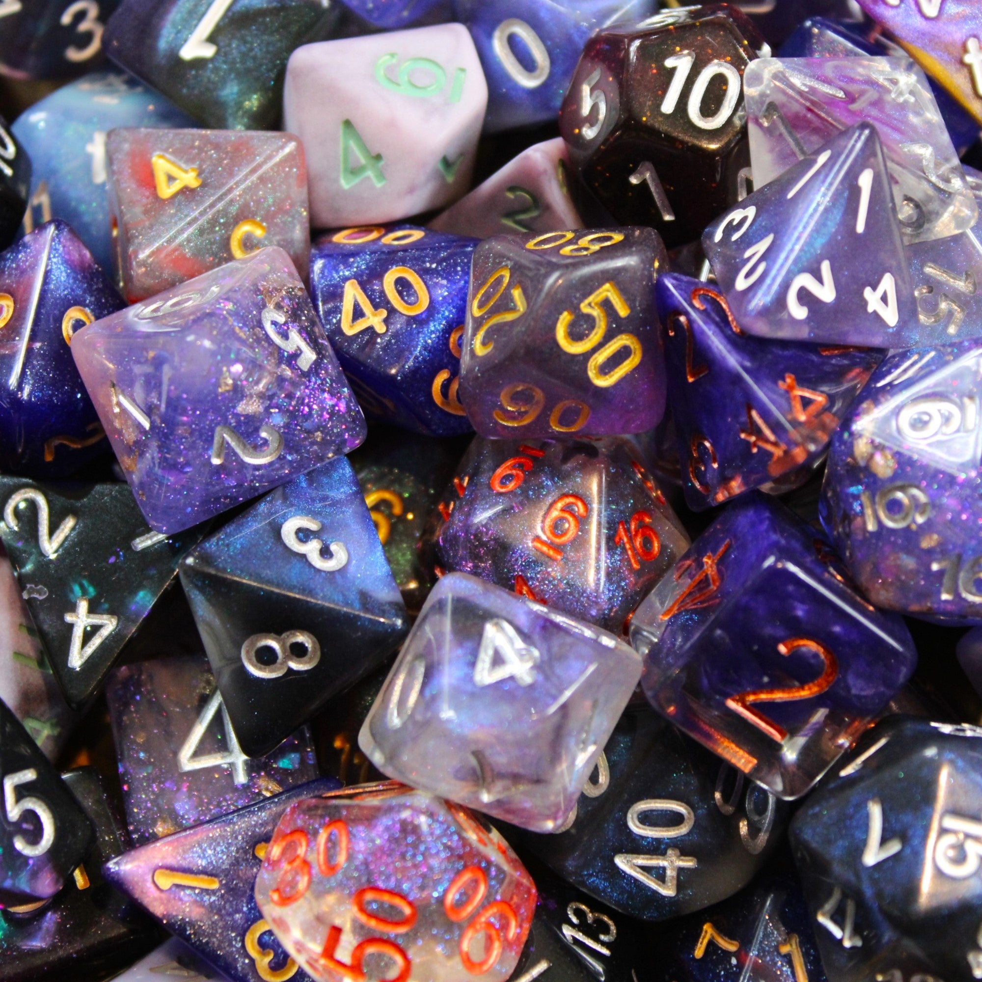Assorted purple glitter, transparent and solid DnD polyhedral roleplaying dice with different coloured numbers in a pile.