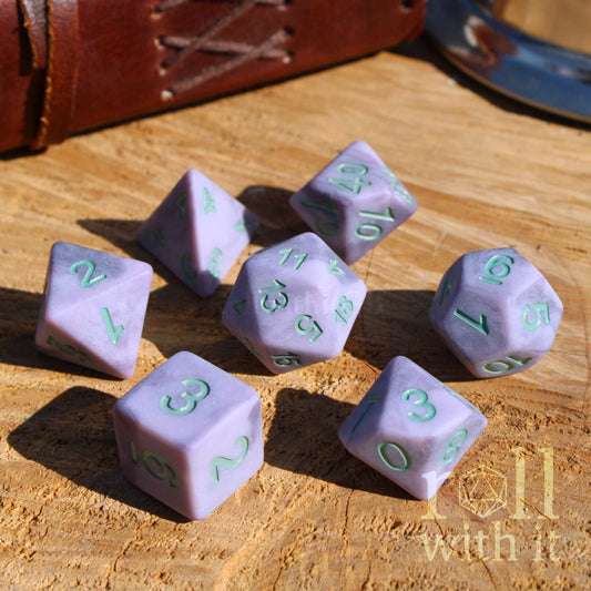 Purple lilac polyhedral dice with matte silver grey numbers on a wooden surface