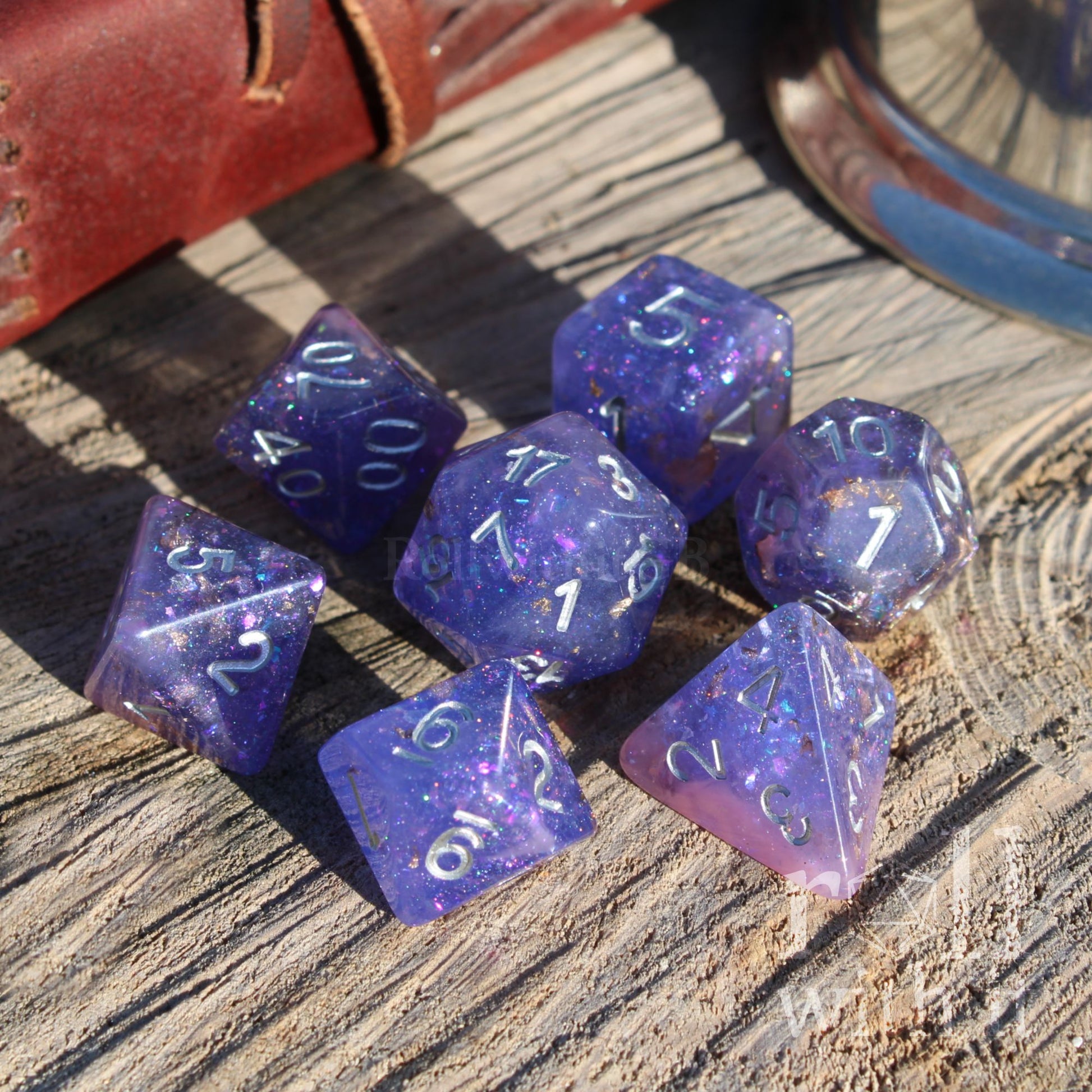 Purple polyhedral dice set on a wooden surface with a leather book and metal object in the background.