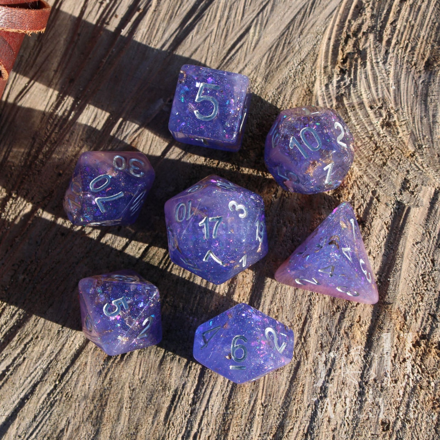 Set of layered purple pink gold leaf shiny reflective polyhedral dice on a wooden surface with silver numbers