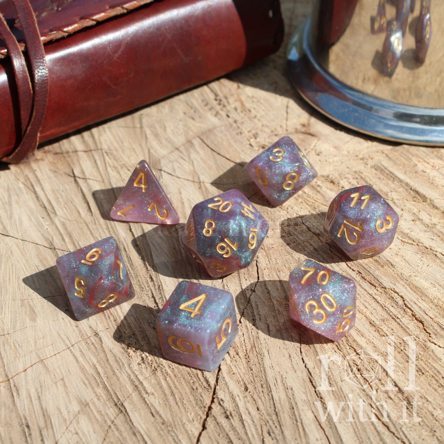 Set of purple polyhedral dice with gold numbers on a wooden surface, with a leather-bound book and metal container in the background.