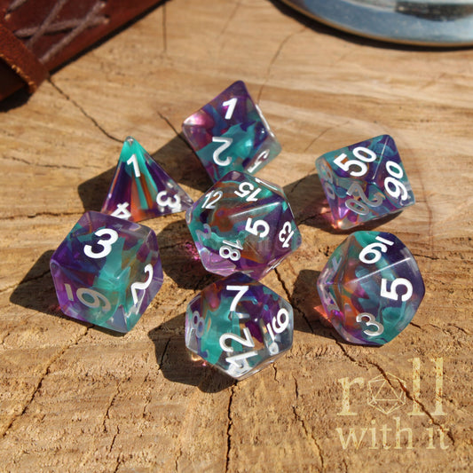 Set of colorful ribbon swirling rainbow blue purple polyhedral dice on a wooden surface with 'roll with it' branding.