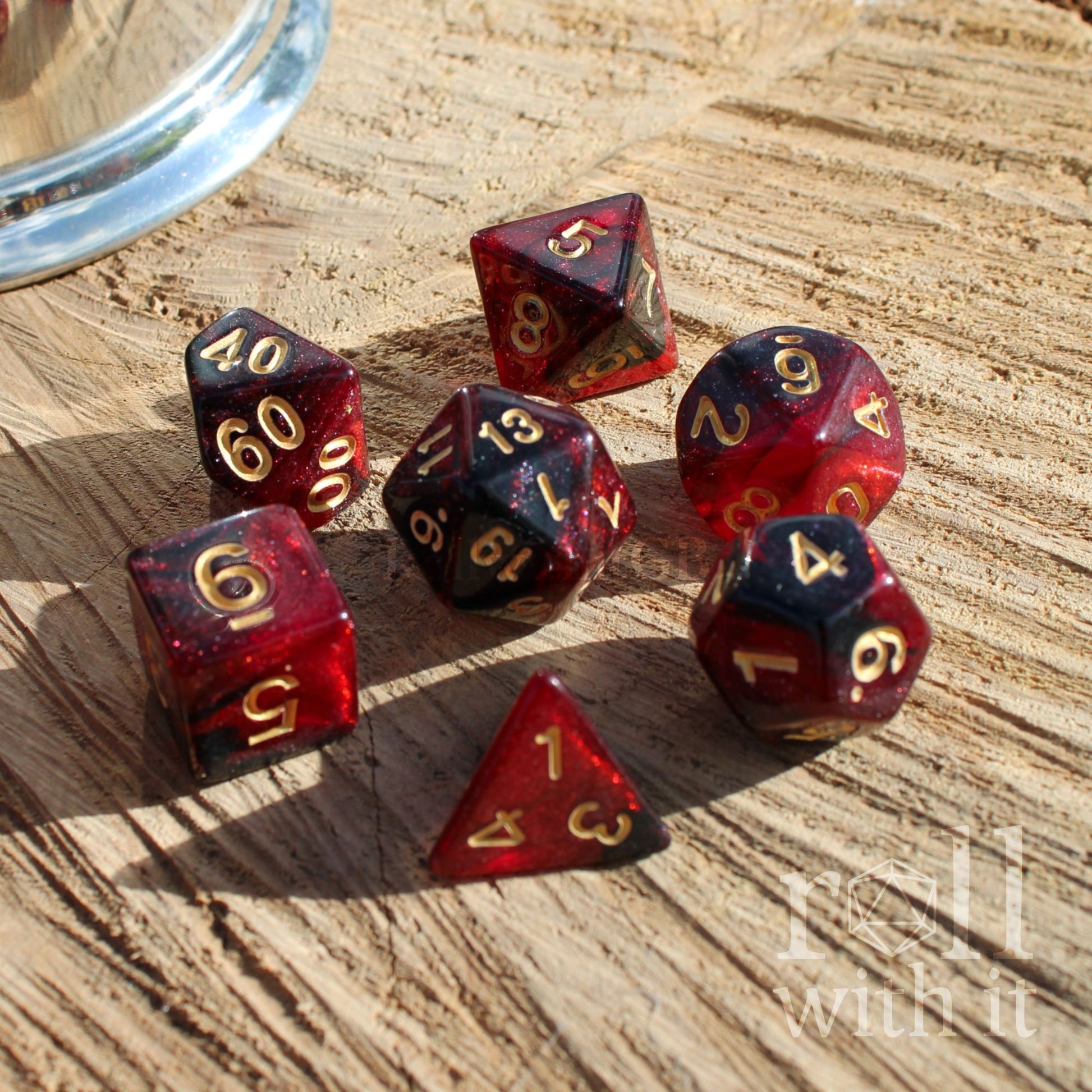Set of red and black polyhedral dice on a wooden surface with 'Roll with It' text.