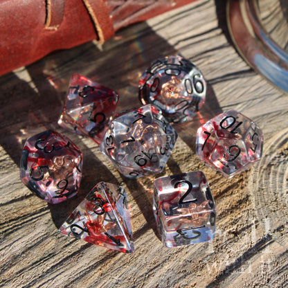 Set of transparent rogue blood dagger dice with red and black numbers on a wooden surface