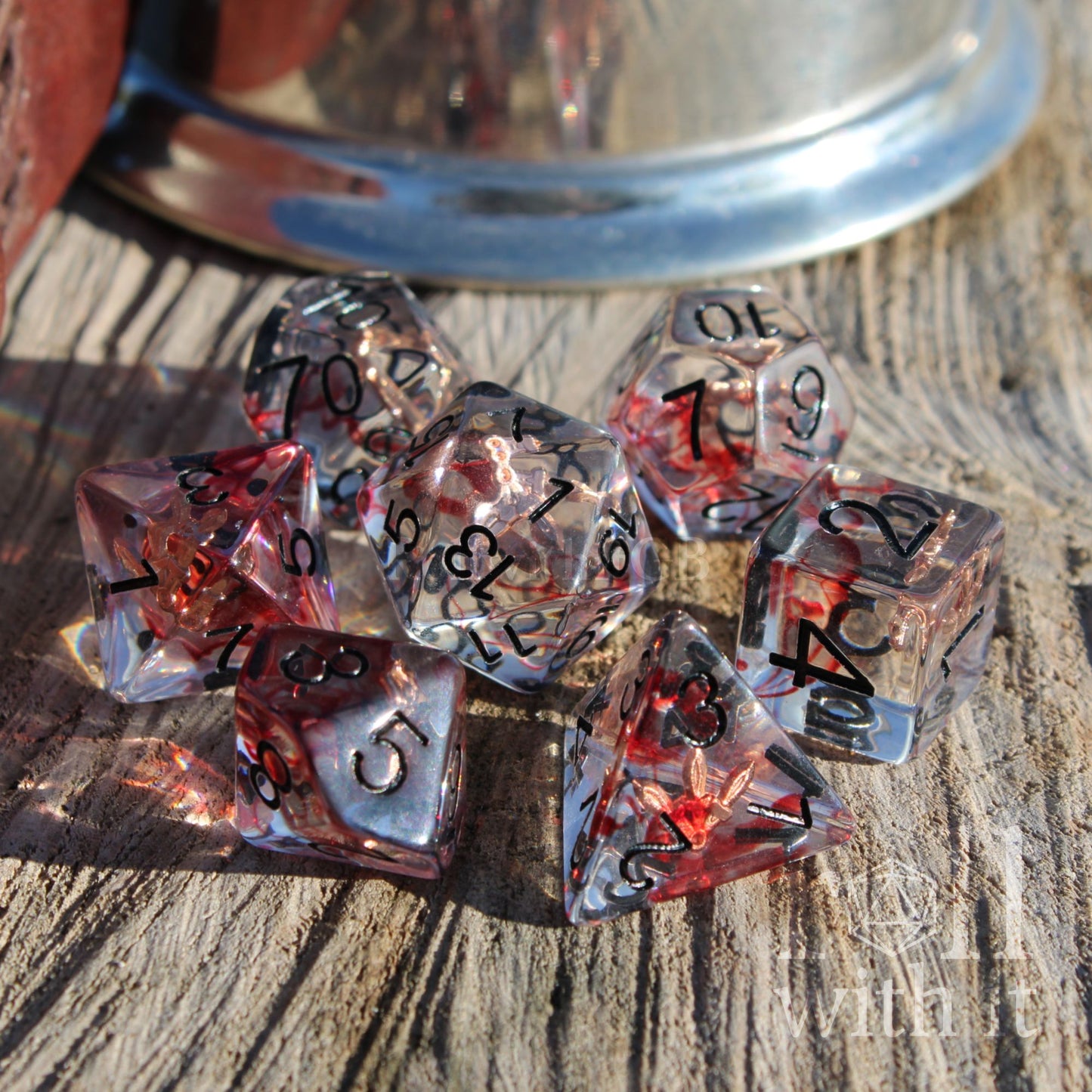 Set of transparent dice with red and black numbers and copper daggers inside clear resin on a wooden surface