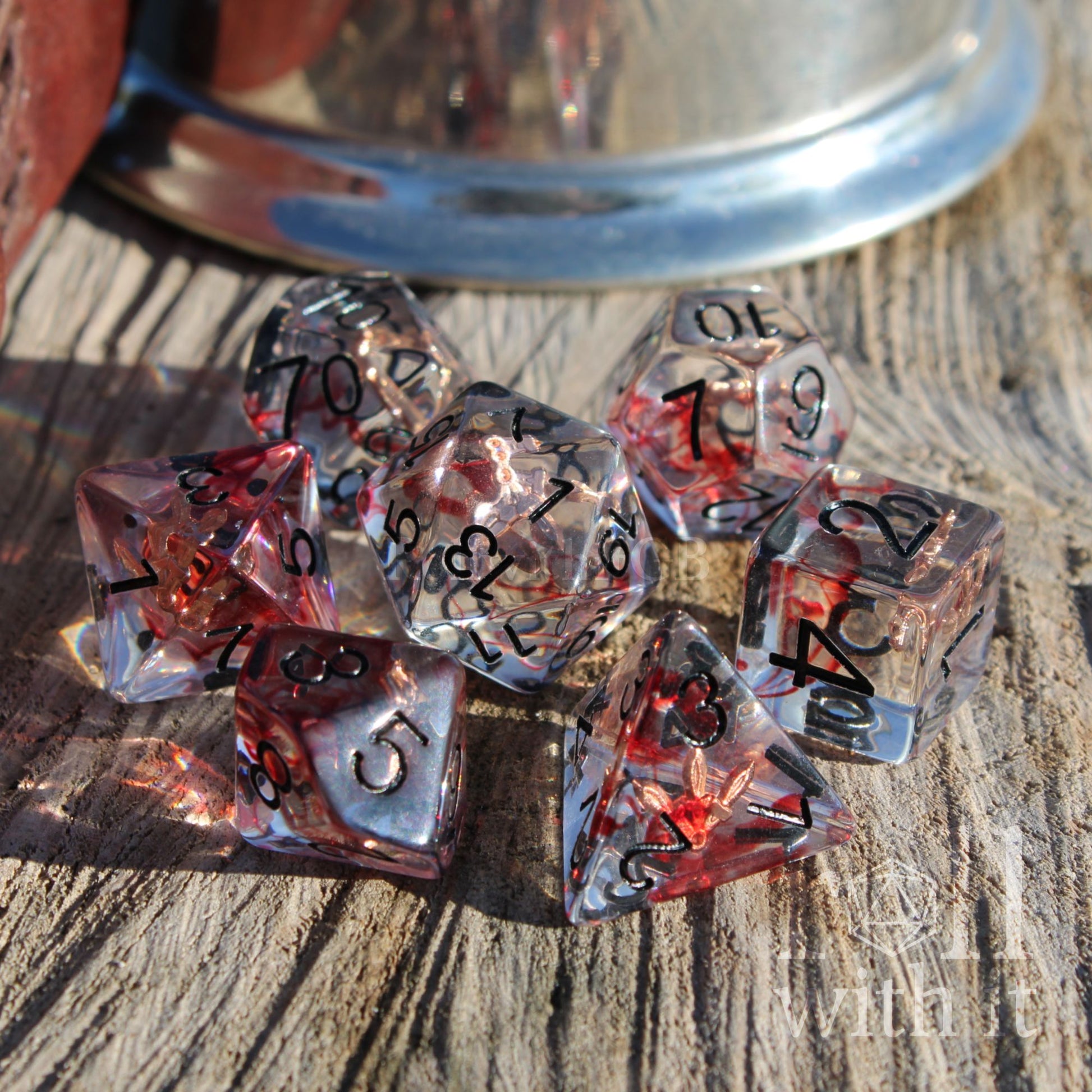 Set of transparent dice with red and black numbers and copper daggers inside clear resin on a wooden surface
