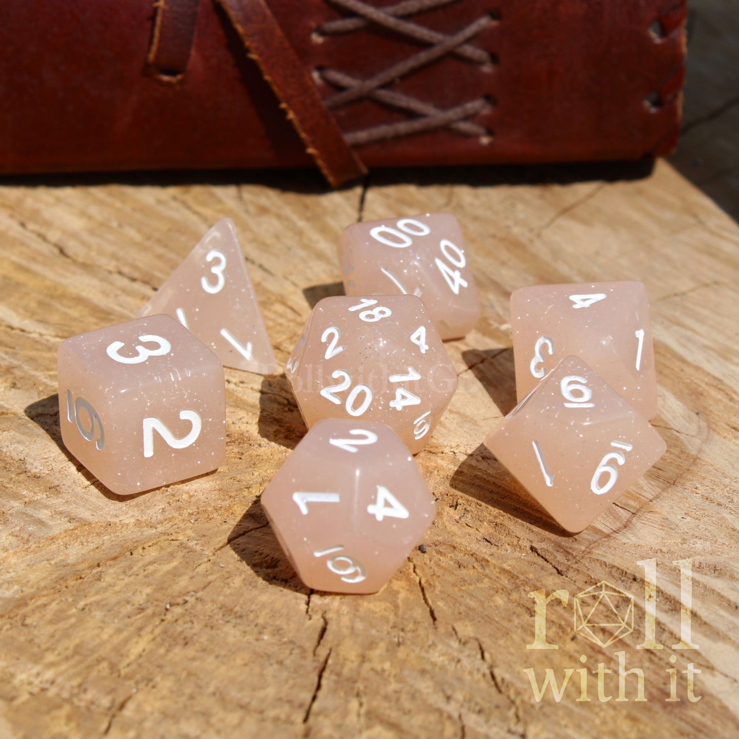 Set of rose coloured dice with white numbers on a wooden surface, featuring 'roll with it' branding.