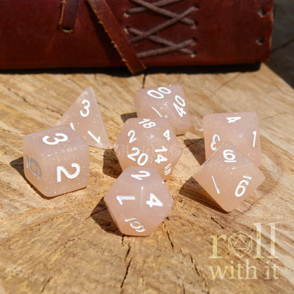 Set of rose coloured dice with white numbers on a wooden surface, featuring 'roll with it' branding.