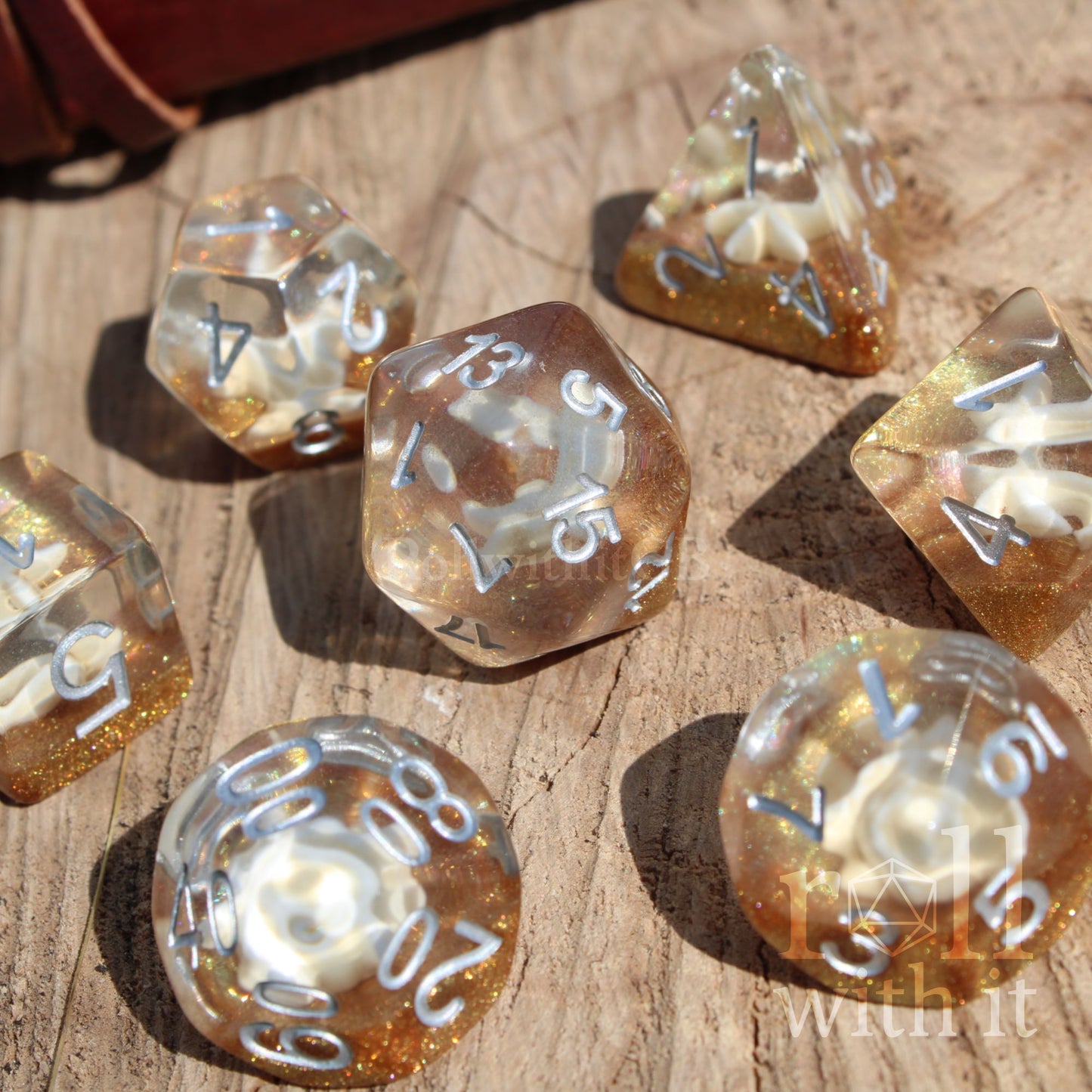 Set of gold and clear glitter filled sea themed beach sandy polyhedral dice on a wooden surface with 'withit' branding.