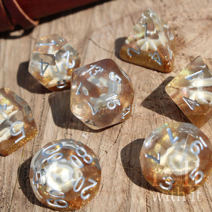 Set of gold and clear glitter filled sea themed beach sandy polyhedral dice on a wooden surface with 'withit' branding.