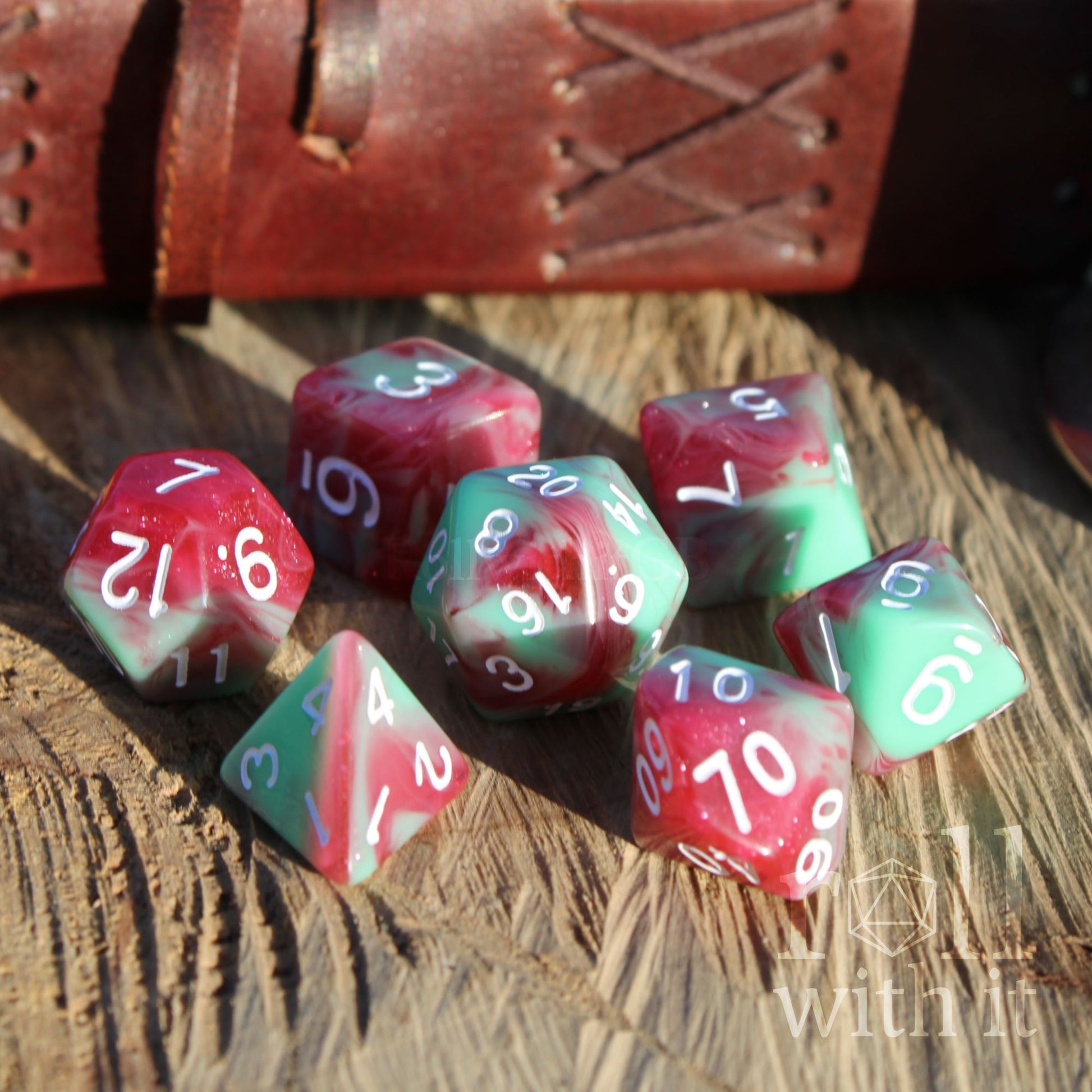 Set of red and green polyhedral dice on a wooden surface with a leather book in the background.