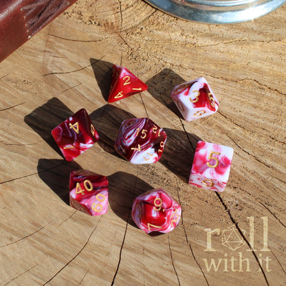 Set of marbled red and pink dice with white streaks on a wooden surface with 'roll with it' text.