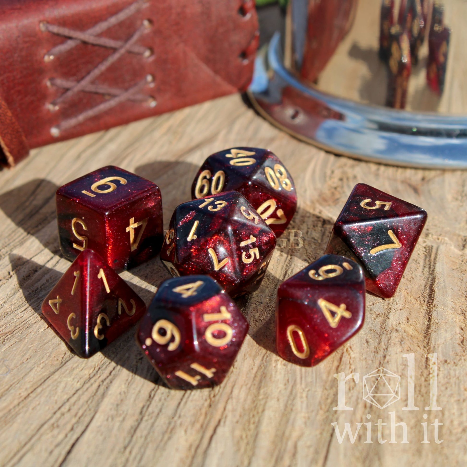 Set of red and black polyhedral dice with gold numbers on a wooden surface, with 'roll with it' text.