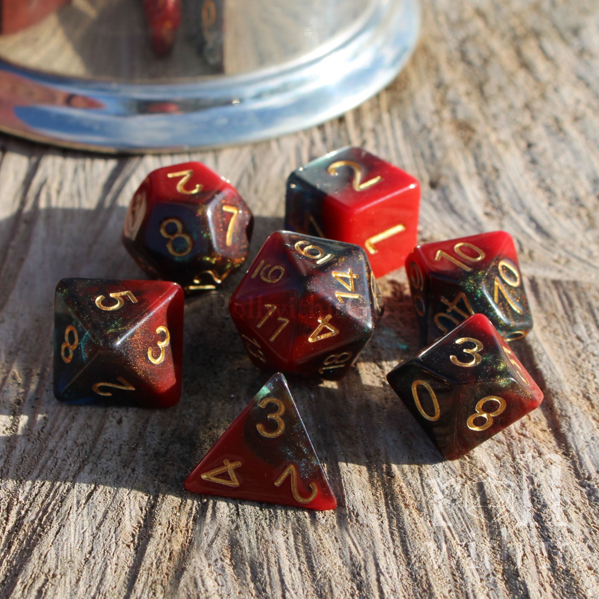 Set of polyhedral bright scarlet black blue dice on a wooden surface with a metallic object in the background.