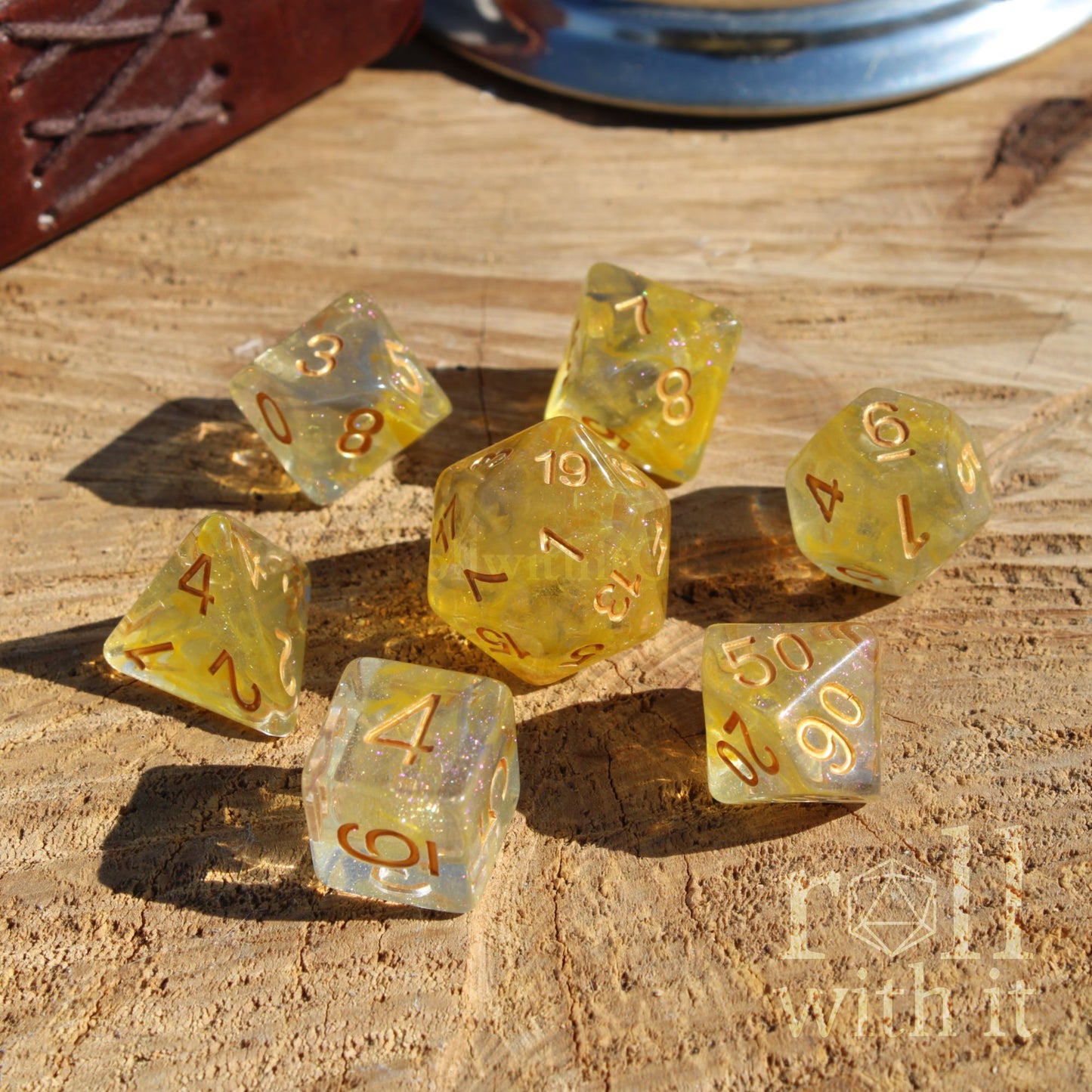 Set of translucent yellow shiny glitter polyhedral dice with numbers on a wooden surface, featuring 'Roll With It' branding.