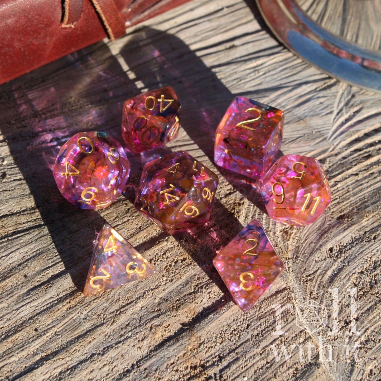 Set of pink and purple foil reflective dice with gold numbers on a wooden surface