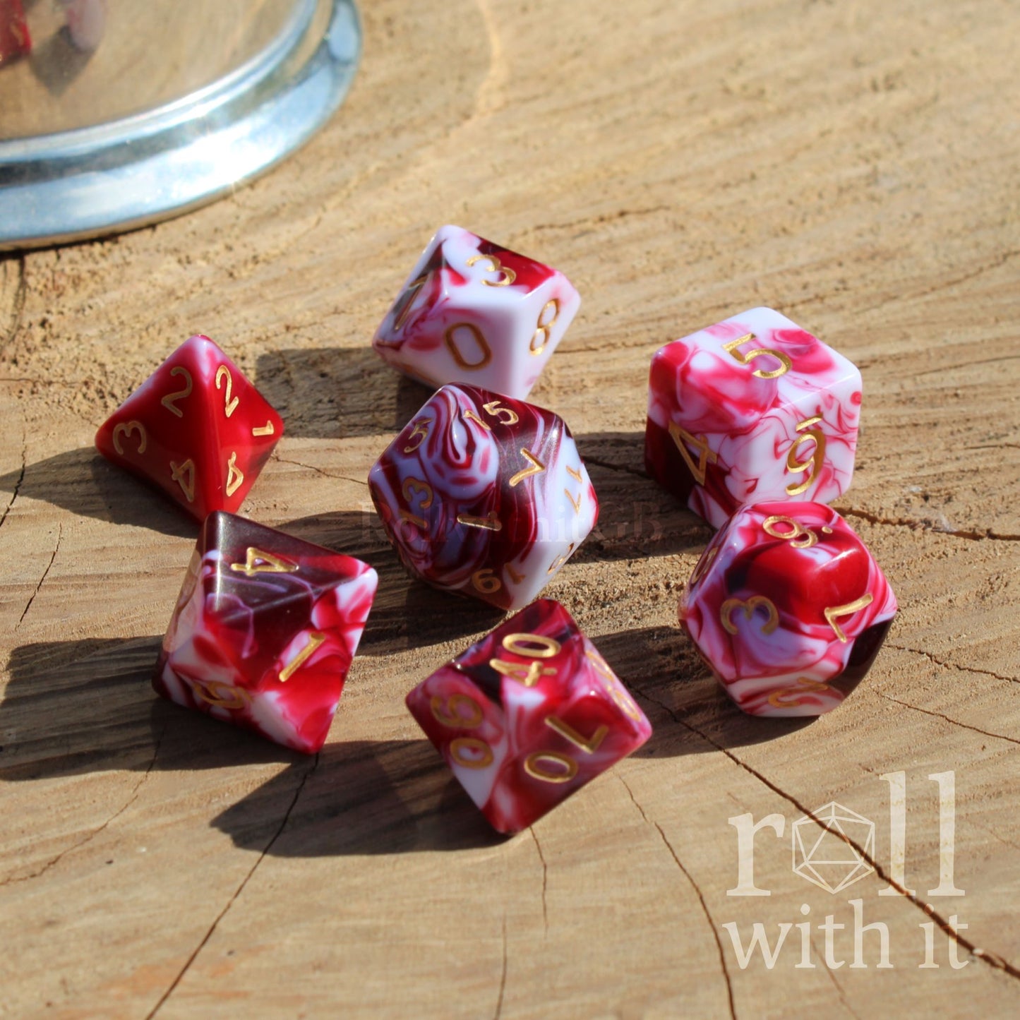 Set of shiny red and white polyhedral dice on a wooden surface with 'roll with it' text.