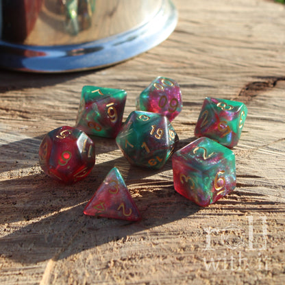 Set of colorful mixed glitter purple green reflective polyhedral dice on a wooden surface with a metallic cup in the background.
