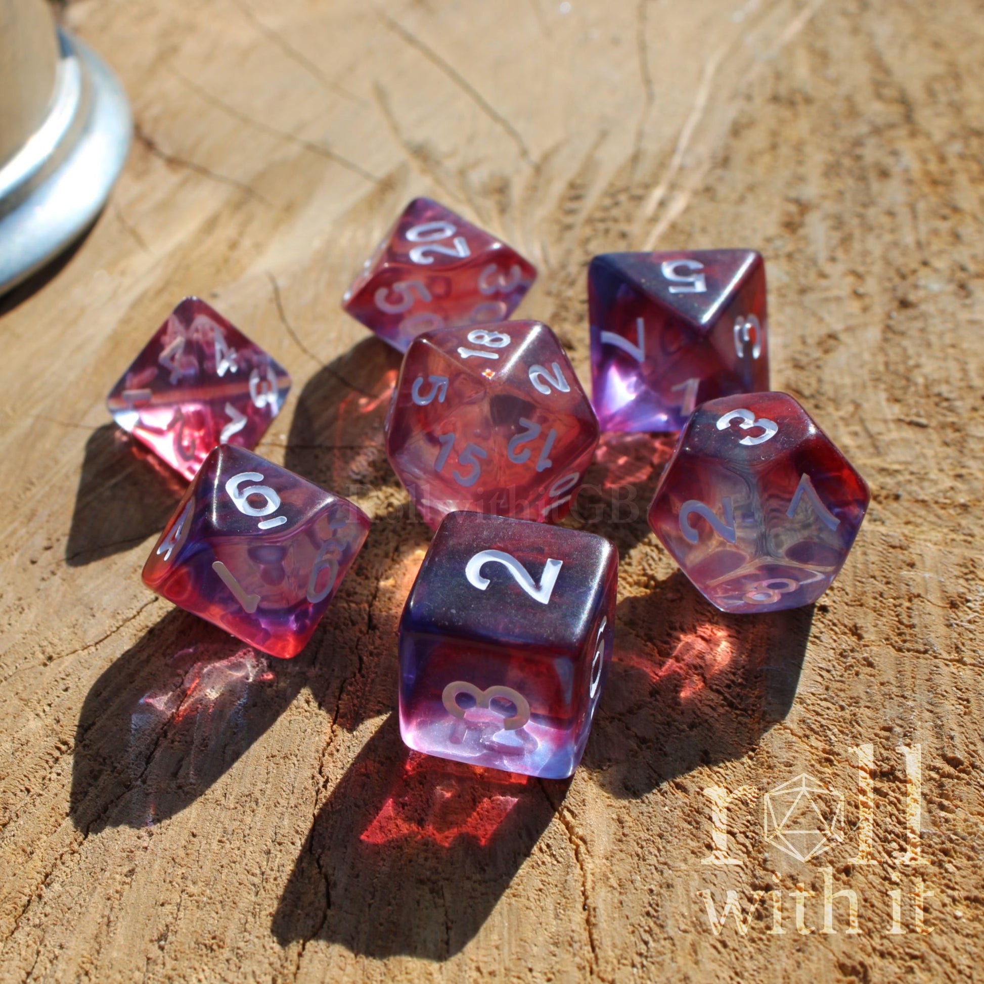 Set of red and purple mixed clear shiny polyhedral dice on a wooden surface with a brand logo in the corner.
