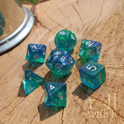 Set of blue and green polyhedral dice with silver numbers on a wooden surface