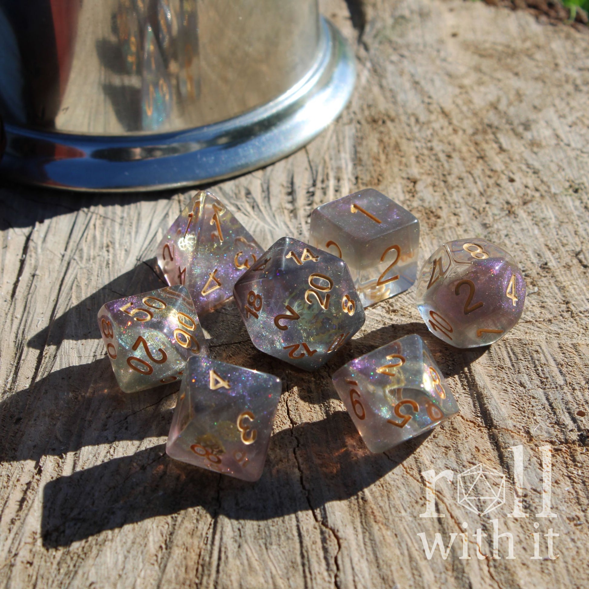 Side angle of 7 polyhedral DND rpg playing dice filled with purple silver and with golden inke numbers and golden gears inside on a wooden surface.