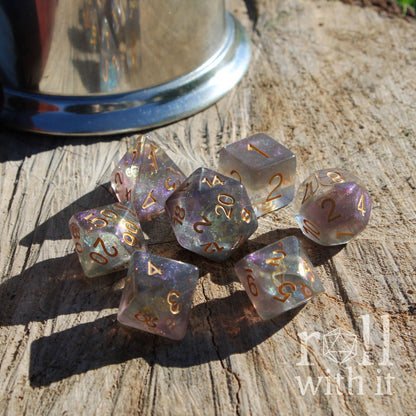 Side angle of 7 polyhedral DND rpg playing dice filled with purple silver and with golden inke numbers and golden gears inside on a wooden surface.