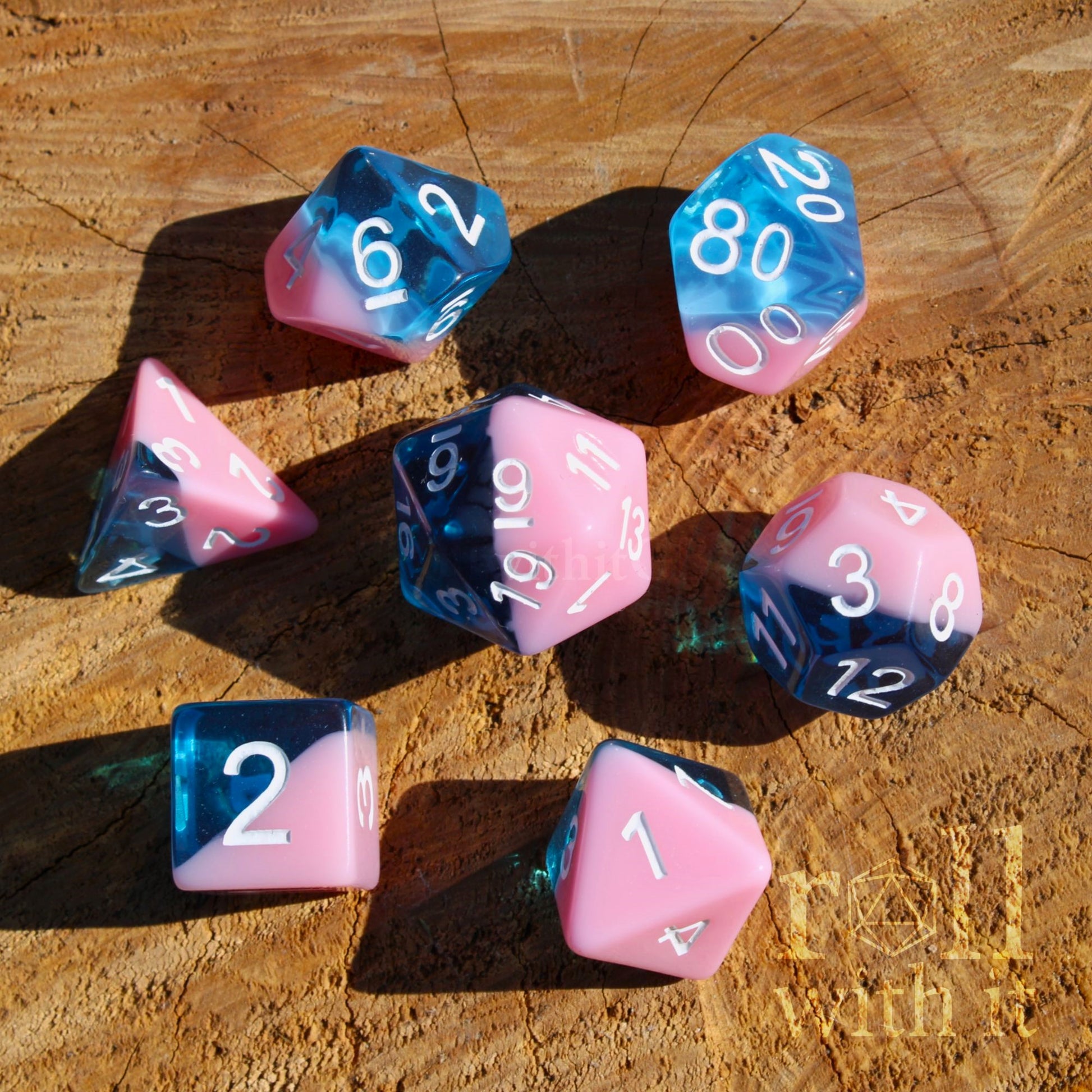 Set of bubblegum pink and clear blue polyhedral roleplaying dice on a wooden surface