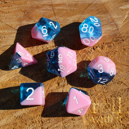 Set of bubblegum pink and clear blue polyhedral roleplaying dice on a wooden surface