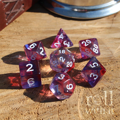 Set of red and purple mixed swirling clear polyhedral dice on a wooden surface with 'roll with it' branding.