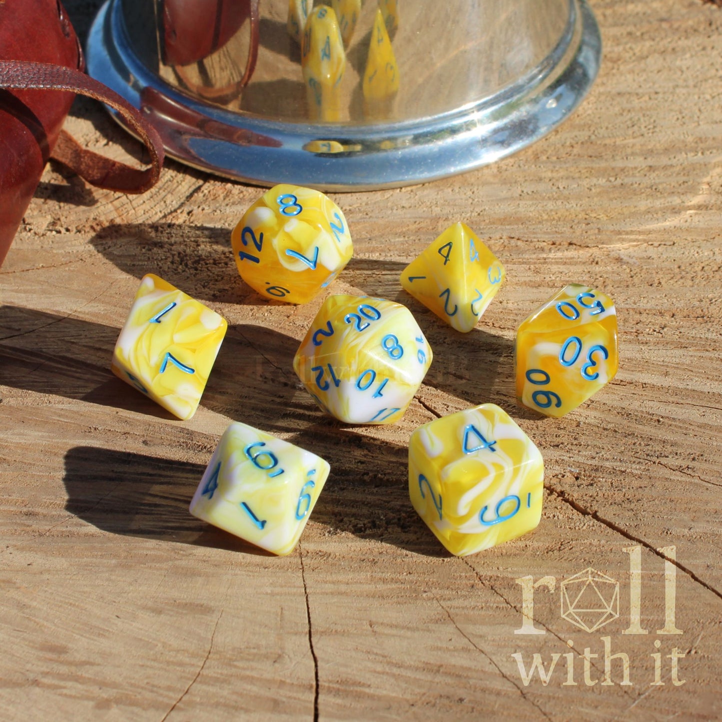 Yellow mixed swirling dnd dice with blue numbers on a wooden surface, featuring the 'roll with it' brand.