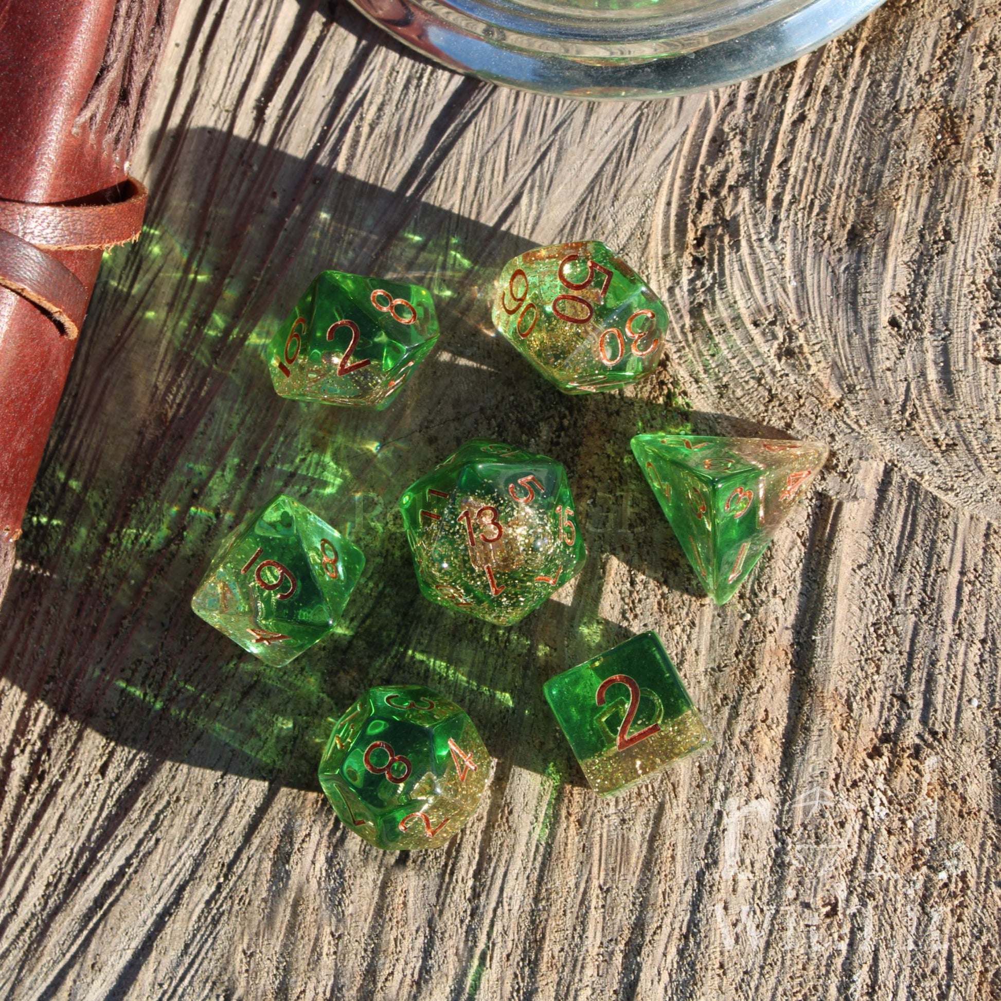 Set of transluscent green gold glitter filled polyhedral dice with copper accents on a wooden surface.