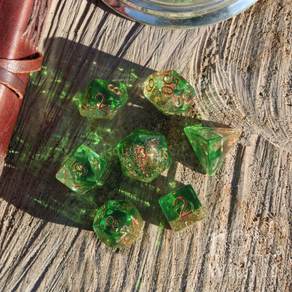 Set of transluscent green gold glitter filled polyhedral dice with copper accents on a wooden surface.