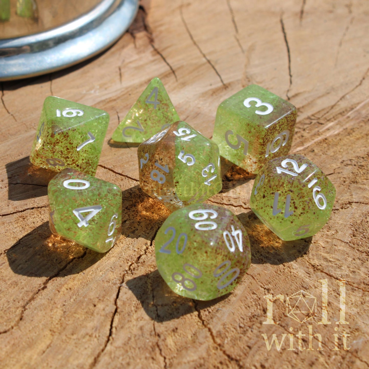 Set of green orange polyhedral dice on a wooden surface with 'roll with it' text.