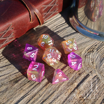 Set of colorful polyhedral dice on a wooden surface with a leather-bound book in the background.