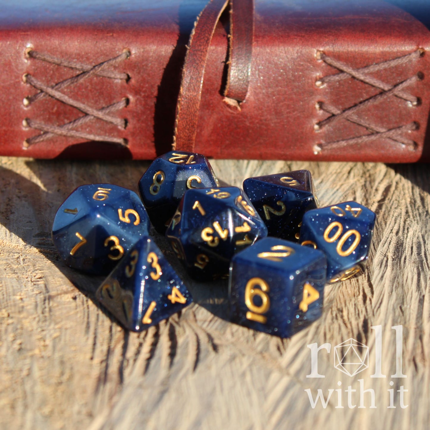 Blue dark skies polyhedral dice set with gold numbers on a wooden surface, next to a leather dice bag.