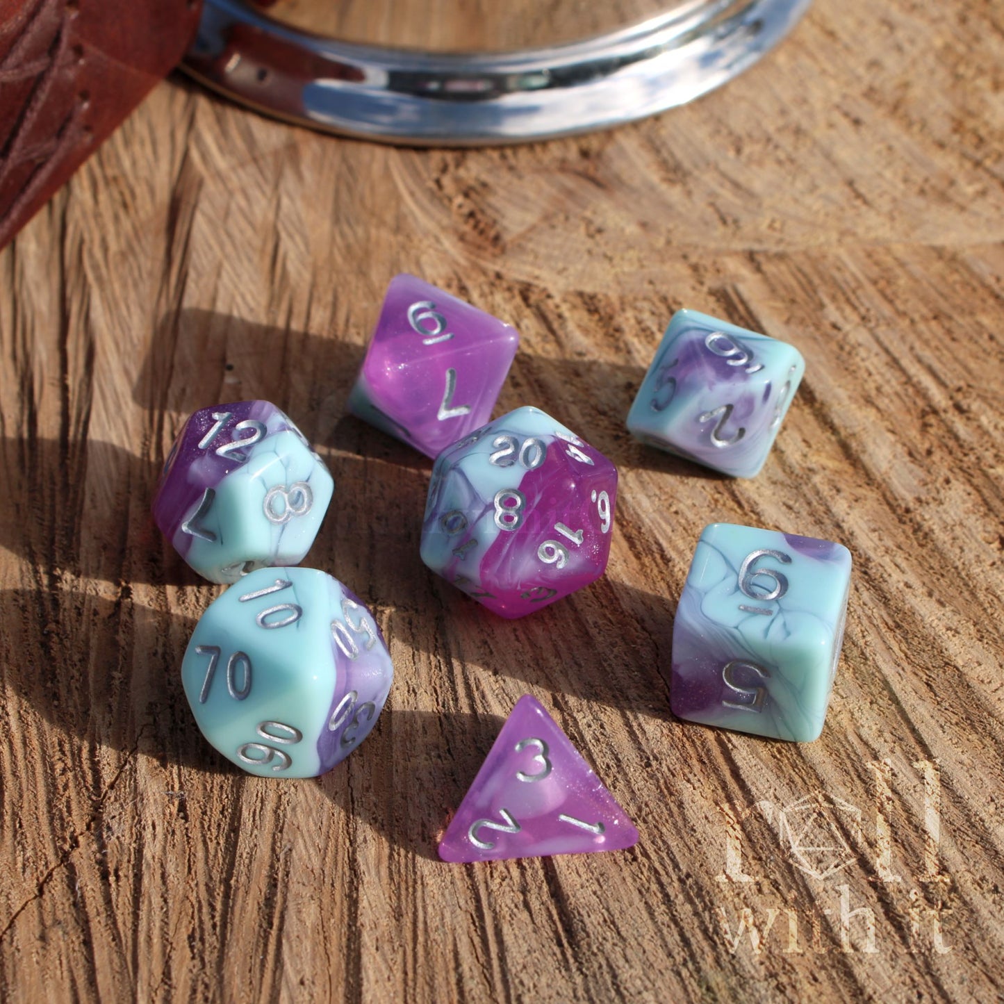 Set of polyhedral dice with purple and pale teal colors on a wooden surface